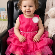 Child in a pink dress sitting on a black chair with a toy in the background