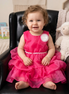 Child in a pink dress sitting on a black chair with a toy in the background