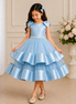 Young girl wearing a light blue dress with ruffled layers in a decorated room.