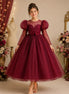 Woman wearing a burgundy lace dress with puff sleeves in a decorated room.