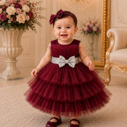 Baby in a burgundy dress with a silver bow in an elegant room.