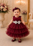 Baby in a burgundy dress with a silver bow in an elegant room.