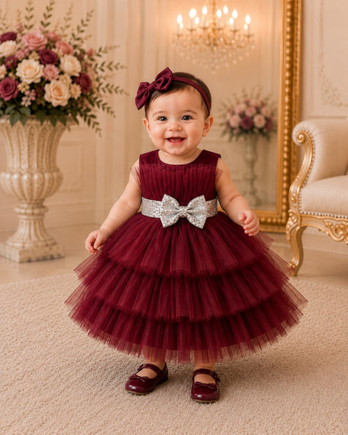 Baby in a burgundy dress with a silver bow in an elegant room.