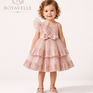 Young girl wearing a pink sequined dress with a bow, standing against a white background with 'Royavelle' branding.