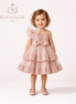 Young girl wearing a pink sequined dress with a bow, standing against a white background with 'Royavelle' branding.