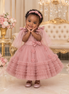Young girl in a pink dress with floral details standing in an elegant room.