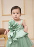 Baby in a light green dress standing indoors with a neutral background