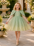 Young girl in a green dress with a cape standing in a garden setting.