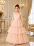 Young girl in a peach lace dress standing in an elegant room with chandelier and floral arrangement.