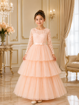 Young girl in a peach lace dress standing in an elegant room with chandelier and floral arrangement.