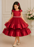 Young girl wearing a red dress with a floral headband, standing in a decorated room.
