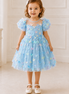 Young girl wearing a light blue dress with butterfly patterns in a bright room.